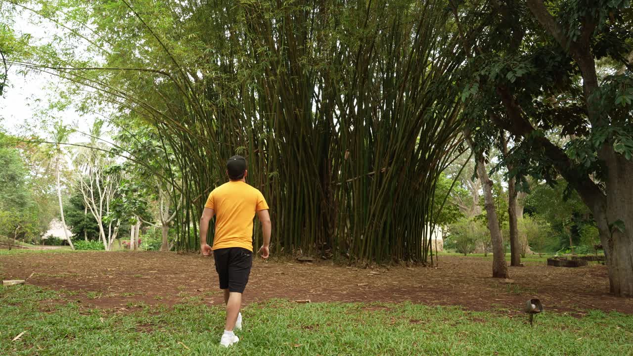 Man in an orange shirt walks toward a massive bamboo grove in a lush green park at a hotel in Yucatan, Mexico.