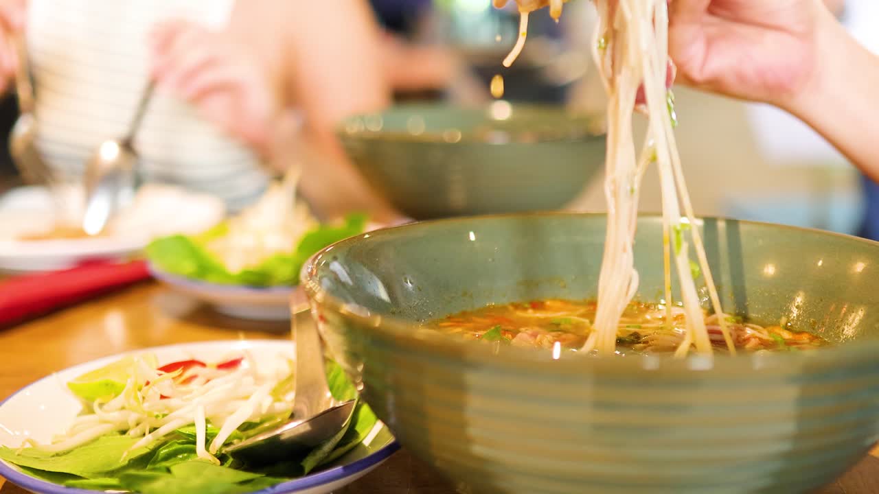 Diners savor Vietnamese pho with chopsticks in a vibrant Bangkok restaurant, highlighting cultural cuisine and lively dining atmosphere