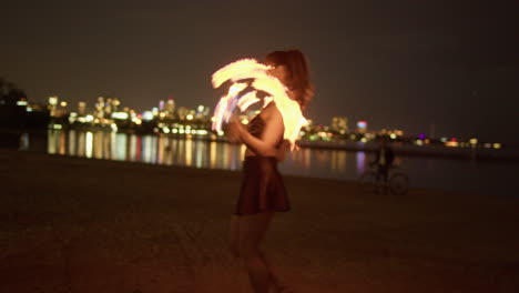 mujer girando ventiladores de fuego en la playa a orillas del lago contra el horizonte de toronto, tiro medio exterior nocturno