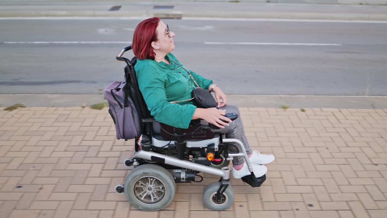 Glad kvinna i elrullstol rör sig på trottoaren
