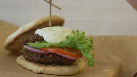 Primer-Plano-De-Una-Hamburguesa-Vegetariana-Gourmet-En-Un-Bollo-De-Pan-Plano-Mientras-Se-Rocía-Con-Salsa