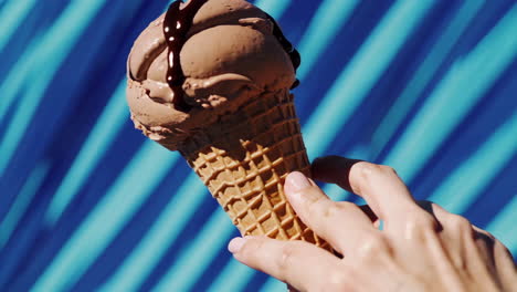 hand holding a chocolate ice cream cone with chocolate syrup drizzle
