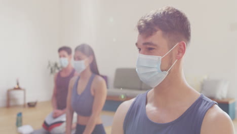 grupo diverso de hombres y mujeres con máscaras faciales arrodillados en esteras en la clase de yoga escuchando al instructor