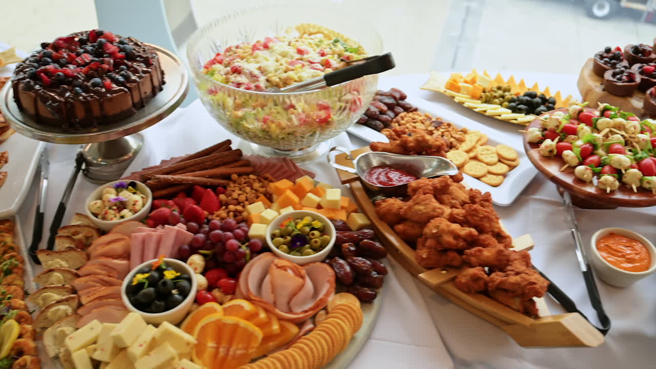 Elegant buffet table with desserts, fruits, and snacks. Catering setup with fruits, pastries, cakes, and appetizers on a white tablecloth for party or event