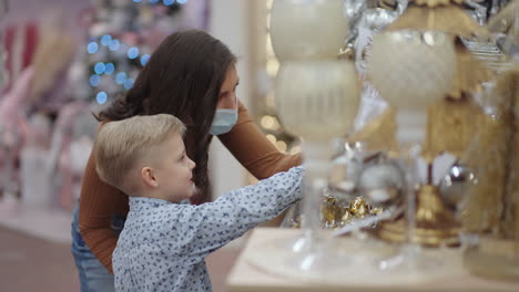 a mother in a medical mask with her son in a shopping center chooses home decorations for christmas