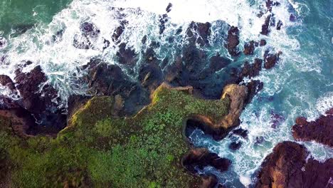 waves crash against jagged rock cliffs on california coast at sunrise