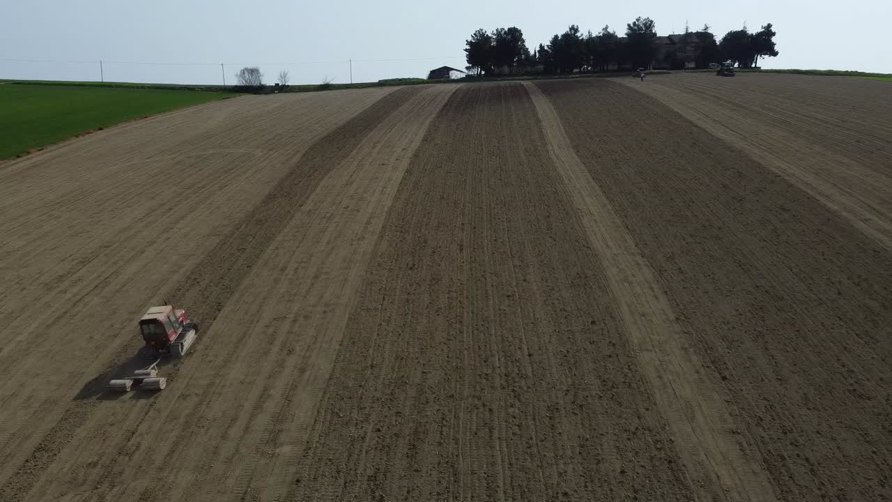 Luftaufnahme von Landwirtschaft: Roter Traktor fährt bergauf mit Bodenwalzgerät, das das Land für die Aussaat vorbereitet