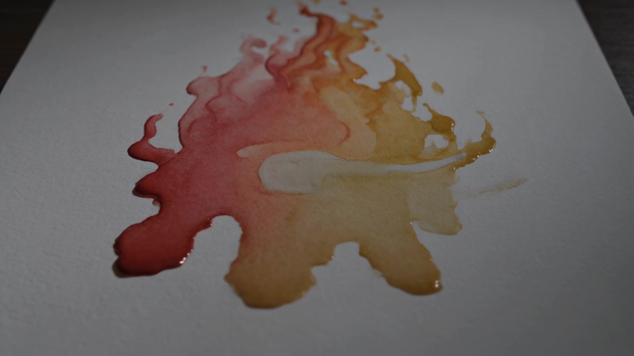 Pigmento rosso-giallo fiamma che si diffonde a contatto con carta bianca su un tavolo scuro, assorbendosi per capillarità.