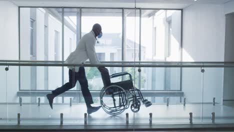 Afroamerikanischer-Männlicher-Oberarzt-Mit-Rollstuhl,-Der-Auf-Dem-Flur-Des-Krankenhauses-Läuft