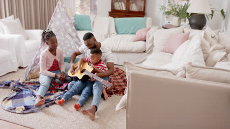 happy african american father, son and daughter playing guitar in living room, slow motion