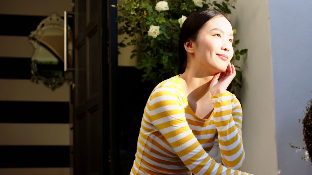 Smiling woman in striped shirt sitting outdoors, enjoying sunlight and nature