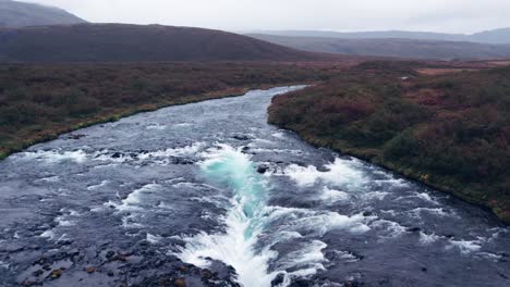 aerial: reverse reveal bruarfoss cascading waterfall off the golden circle in southern iceland that is very picturesque with the beautiful blue cascade of falls into the plunge pool below