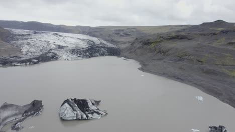 aerial view over the solheimajokull glacier lagoon, in cloudy iceland - reverse, drone shot