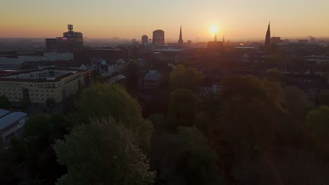 dortmund city skyline at sunrise, drone flying slowly over westpark towards backlit skyline