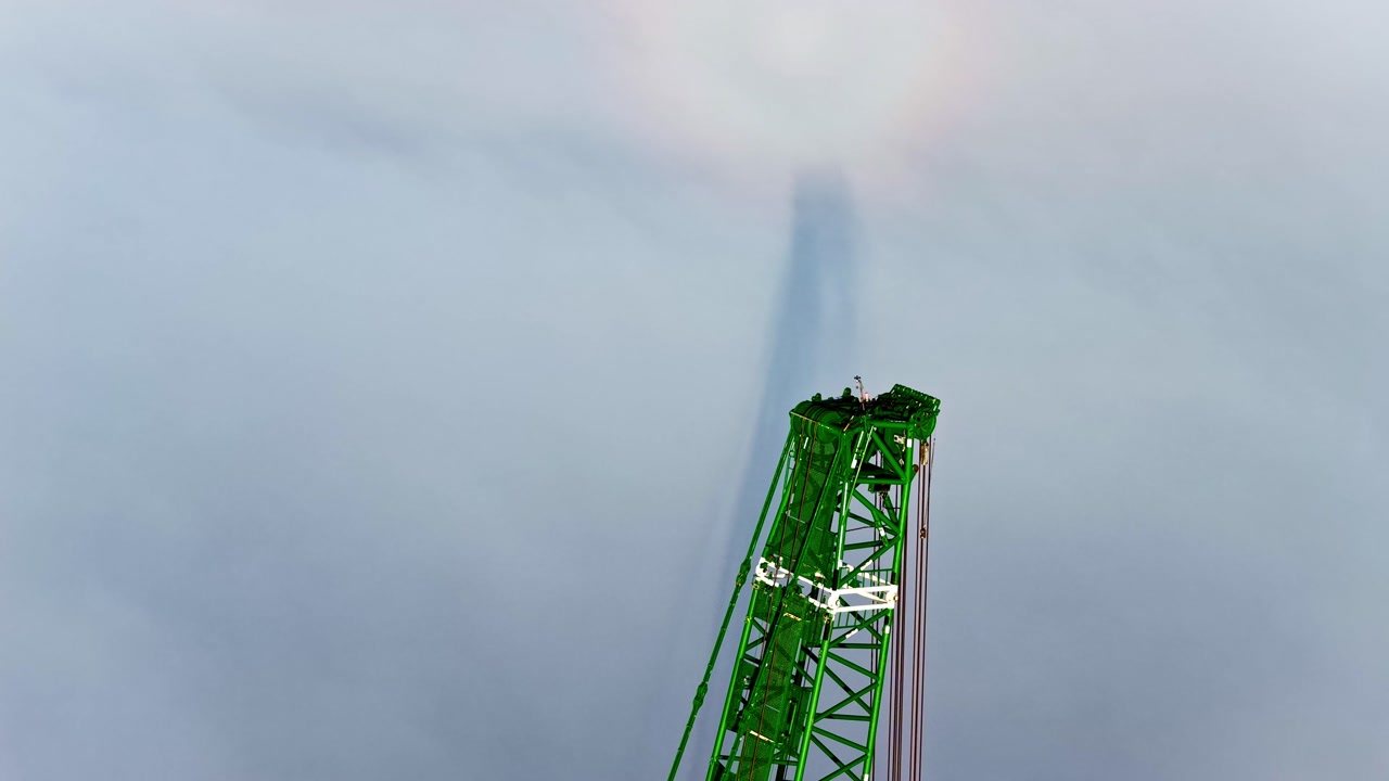 Green crane towering against a cloudy sky, showcasing construction energy