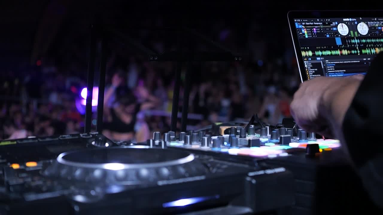 DJ mixing music at concert with audience in background and flashing lights