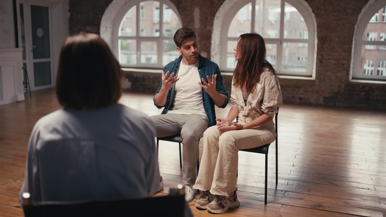 A couple at a reception with a psychologist: a brunette girl and a brunette guy in a denim jacket who expressively talks about their dissatisfaction. Couple therapy with a psychologist