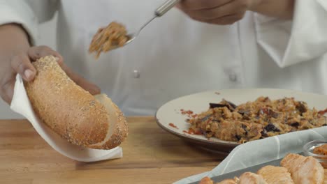 professional chef cook putting fresh salad, cucumber, tomato and onion while making delicious burger. close up of male hands in black gloves. culinary concept