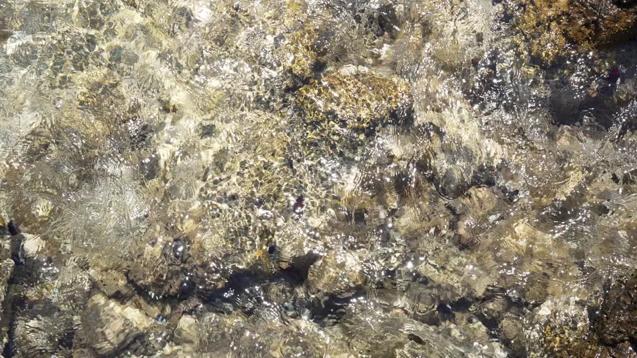 Sollys glimter på klart, lavt havvand med stenet bund