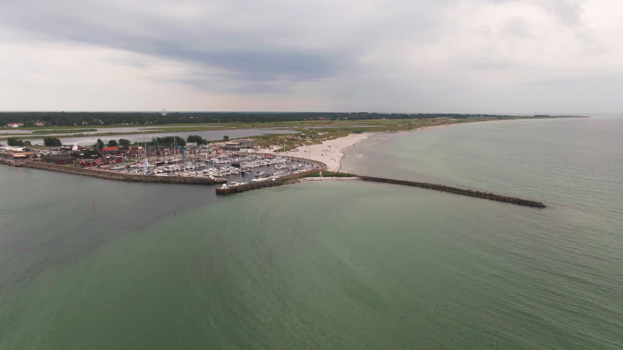 Ampia ripresa aerea con drone dell'ingresso al porto di Skanor con un lungo frangiflutti in pietra e una spiaggia di sabbia bianca