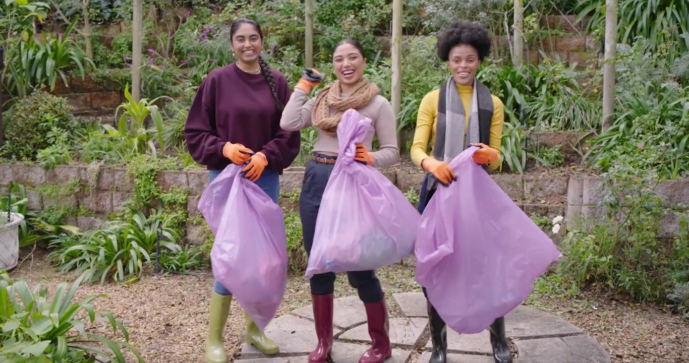Diverse female friends spotting litter, picking on patio with pink bags and gloves cleaning garden