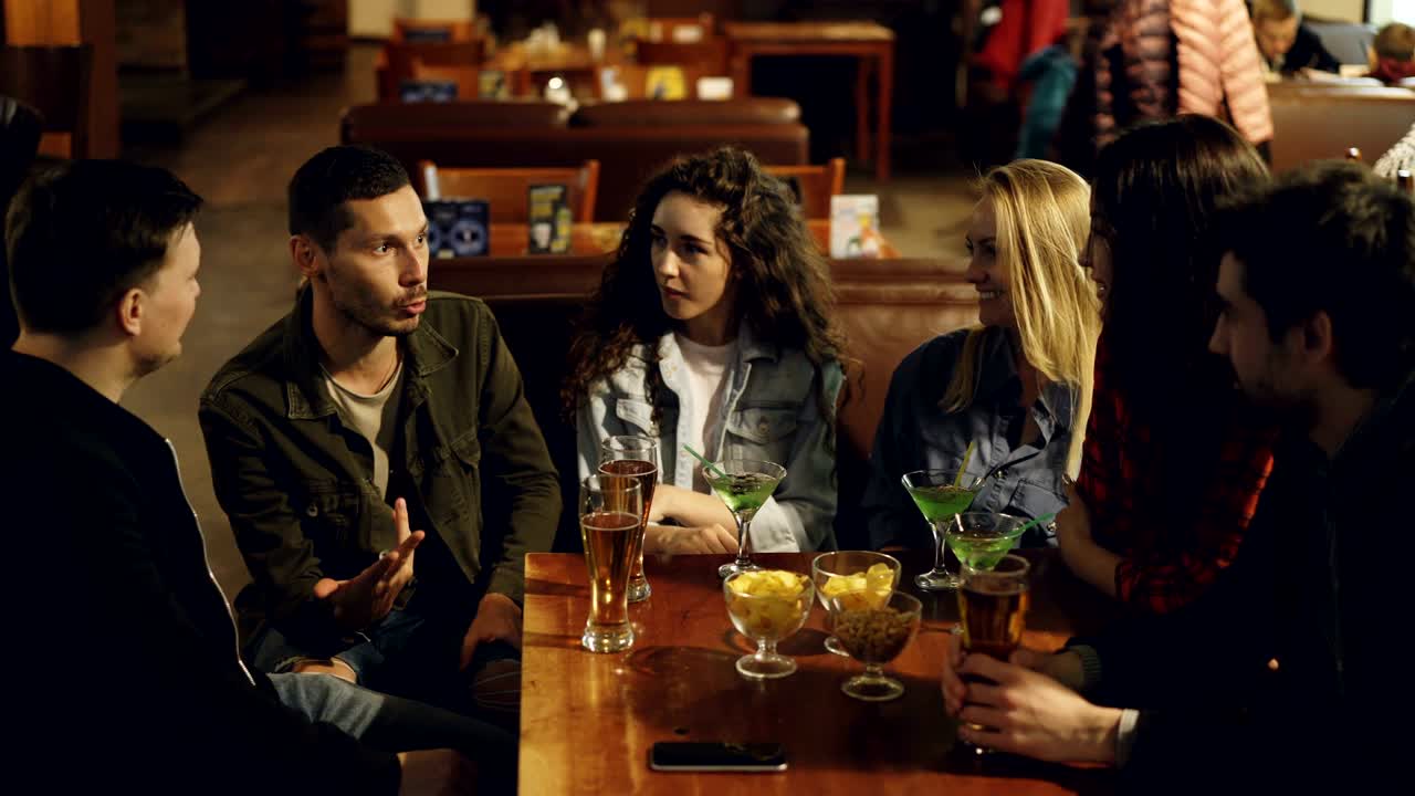 vista de ángulo alto de un joven guapo contando una historia a sus amigos sentados juntos en un café. el tipo barbudo está hablando y gestando, sus compañeros están escuchando y sonriendo.