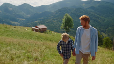 Happy-man-son-walking-on-mountain-slope.-Parent-with-boy-coming-up-green-hill.