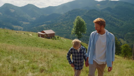 happy man son walking on mountain slope. parent with boy coming up green hill.