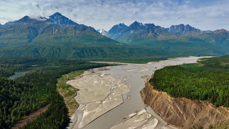 Flight over the wide delta of the shallow river in Alaska wilderness. Gorgeous ridged mountains at backdrop