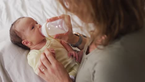 video of happy caucasian mother feeding newborn baby with bottle on bed