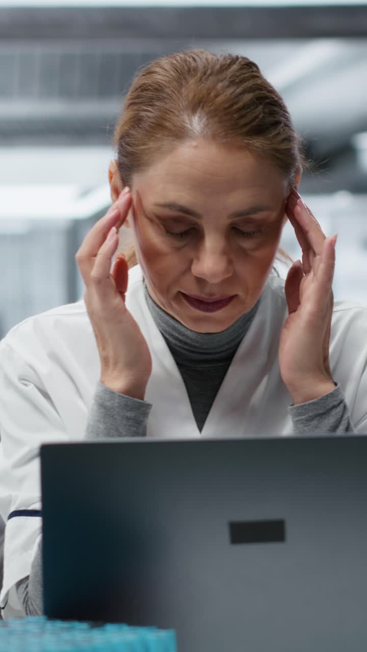 Video verticale Scienziata stanca con mal di testa mentre lavora al computer portatile in laboratorio