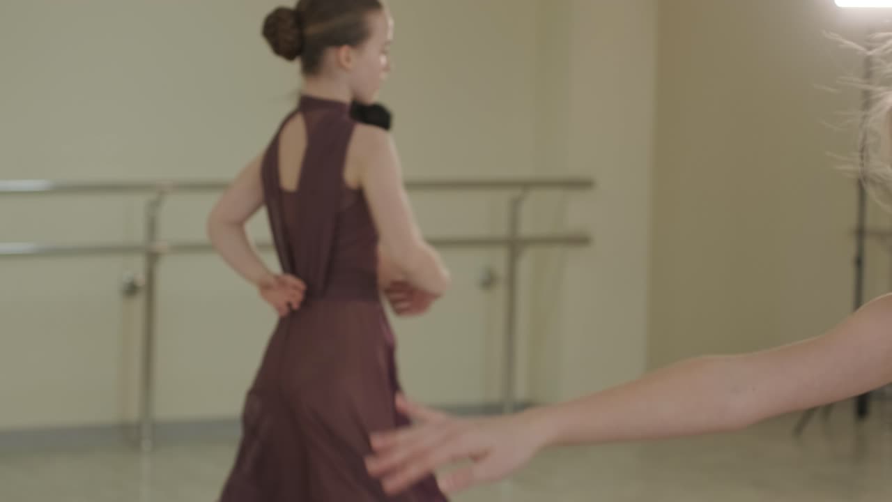 A group of young ballet students in black dancewear practicing positions in a spacious ballet studio with wooden flooring and wall-mounted barres. Focused expressions and synchronized movements.