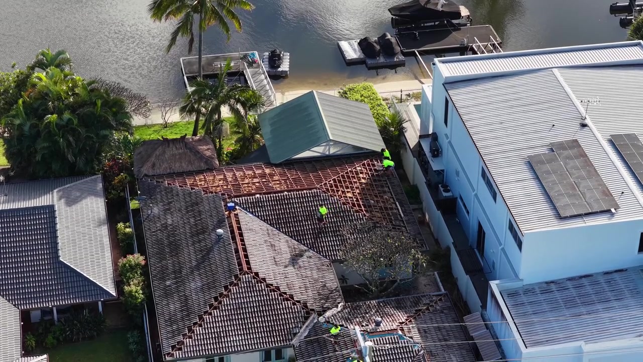 High-angle drone shot of contractors in safety vests working on a waterfront house roof.