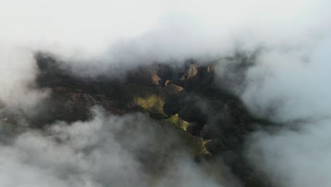 aerial shot peeking through the clouds revealing beautiful green mountain landscape