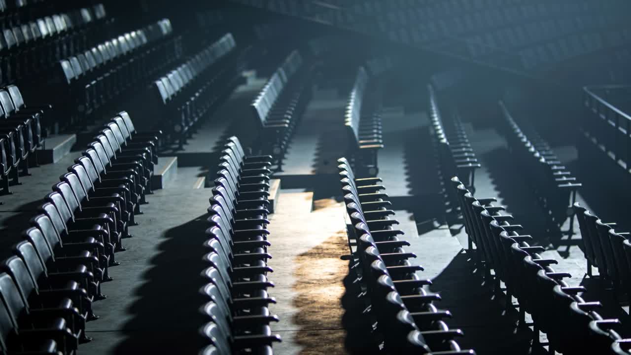 Shifting camera revealing rows of folding seats in arena, highlighting warm light on central aisle