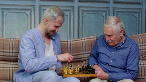 happy different male generations family of senior father and adult son or grandson playing chess