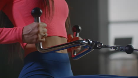 the woman with excellent muscular body pumps her back and shoulder blades on the training machine. she performs three sets ten times for better results.