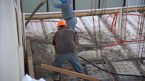 movimiento lento de un par de trabajadores latinos mexicanos aplicando hormigón fresco de una bomba de boom en la estructura de la cuadrícula para hacer la losa de una casa en méxico