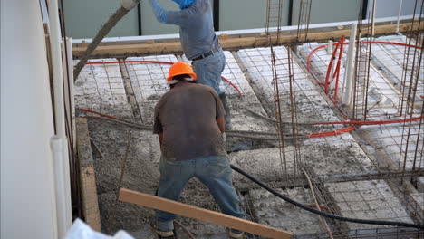 slow motion of a pair of mexican latin workers applying fresh concrete from a boom pump on grid structure to make the slab of a house in mexico