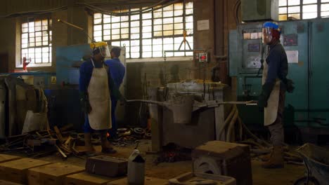 group of workers carrying container of molted metal at workshop 4k