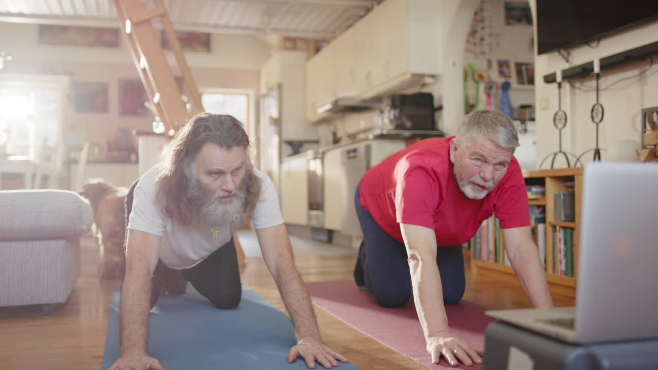 Pair of seniors on all fours follow yoga on laptop attempting child's pose