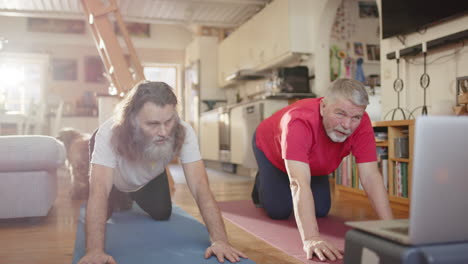 pair of seniors on all fours follow yoga on laptop attempting child's pose