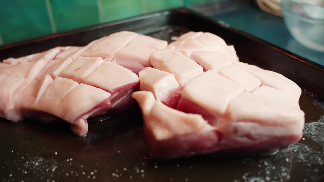 Zwei eingeschnittene Schweinebauchscheiben auf einem Bräter mit Salzgranulaten, bereit zum Backen im Ofen. Nahaufnahme der Essenszubereitung in der Küche mit geringer Schärfentiefe