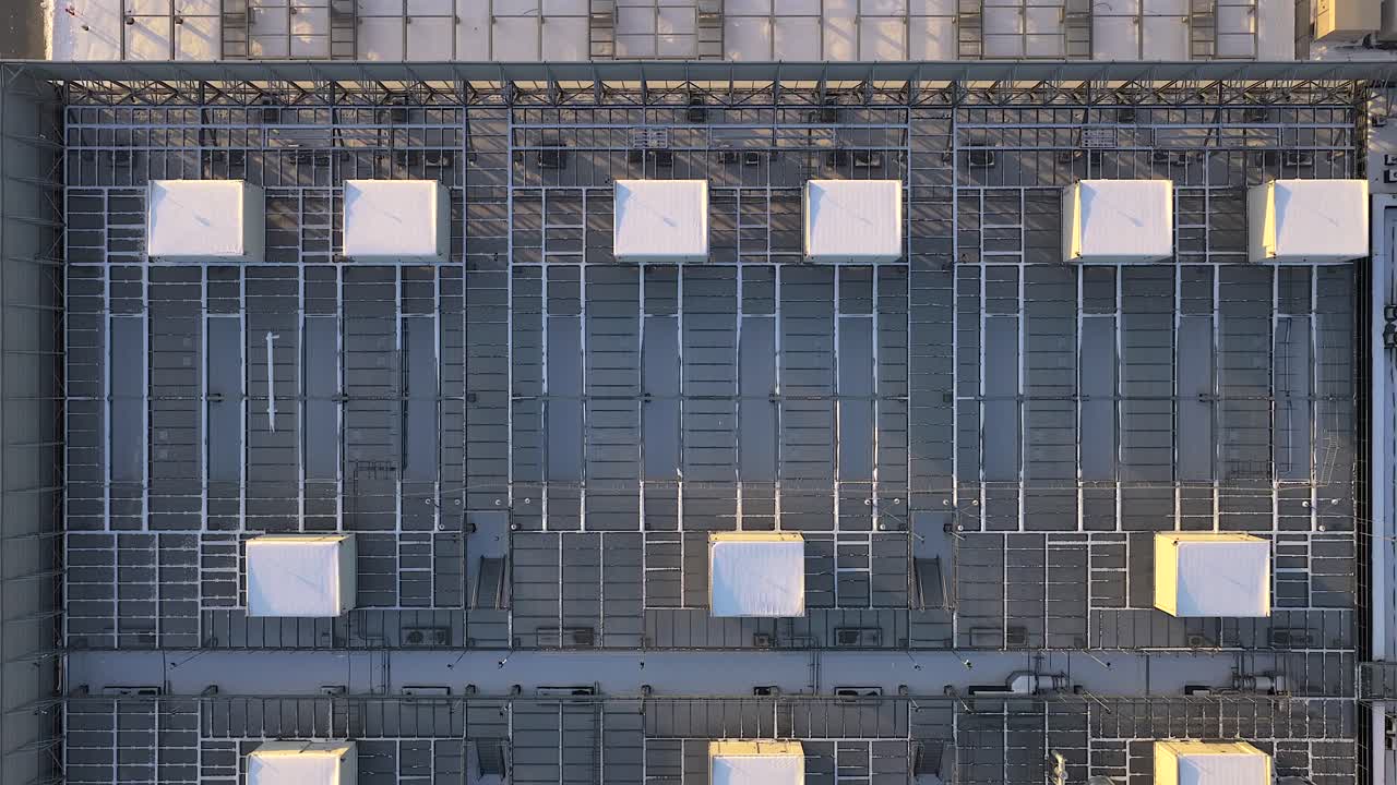Aerial footage moving over the snow covered rooftop of a modern data center building, showing rows of industrial hvac air conditioning units