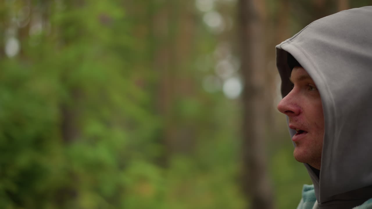 Caucasian hiker pulling hood over head and smiling among pine trunks, adjusting layers and checking gear upbeat microadventure energy, playful preparation and quiet resilience, candid closeups, soft