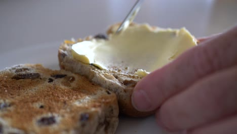 Slow-motion-footage-of-sliced-hot-cross-bun-being-buttered-with-kitchen-knife-on-plate-during-Easter