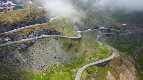 Drone aerial view over Transfăgărășan, winding road, Balea lake lodges, rocky cliffs and mountain mist.