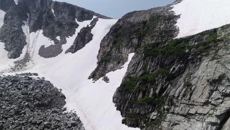 Antena-De-Pico-Cubierto-De-Nieve,-Cerca-Del-Acantilado-Para-Mostrar-Pequeñas-Cascadas-Y-Una-Pequeña-Cueva-De-Hielo