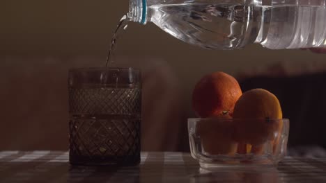 hand pouring fresh water into a glass on a table with fruits slow motion