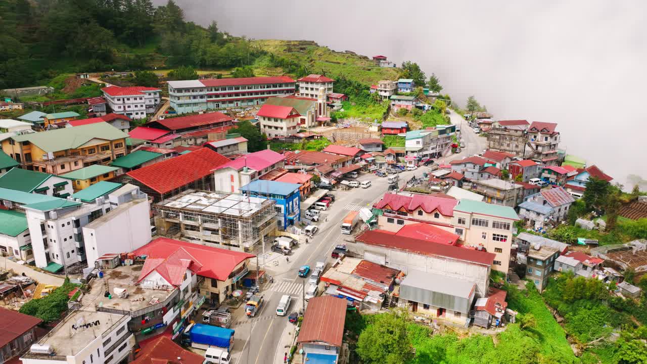 Drone avança sobre a cidade montanhosa de Atok, iluminada pelo sol através de uma chuva passageira.